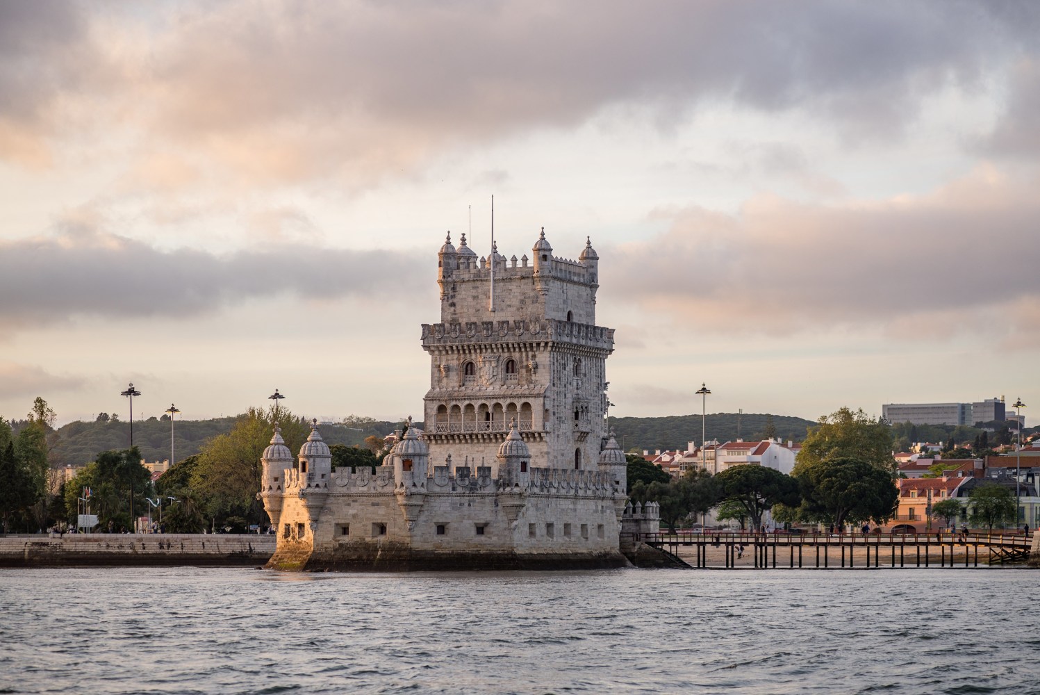 a castle with water in front of a large body of water with Belém Tower in the background